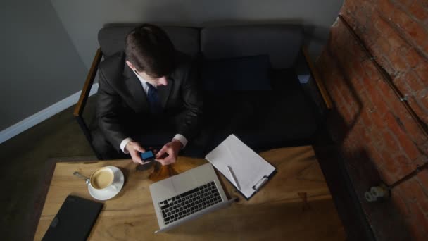 Empresario habla en el teléfono inteligente en la cafetería y trabaja con documentos de negocios. El hombre se sienta a la mesa en la cafetería y habla por teléfono celular, el portátil yace sobre la mesa. vista superior — Vídeo de stock