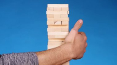 eller genç adam çalış jenga üzerinde mavi arka plan, yakın çekim. Bir adam bir kule bloklar jenga oynarken oluşturur