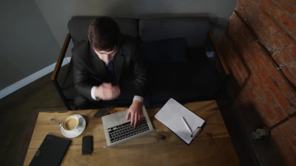 Hombre de negocios cansado trabajando en el ordenador portátil y beber café en la cafetería. vista superior — Vídeo de stock