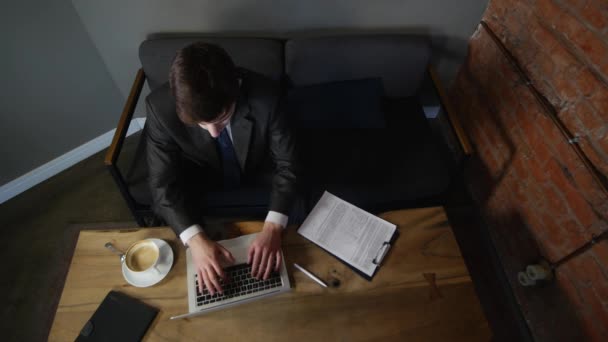 व्यापारी लैपटॉप पर काम करता है और कैफे में दस्तावेजों पर हस्ताक्षर करता है। शीर्ष दृश्य — स्टॉक वीडियो