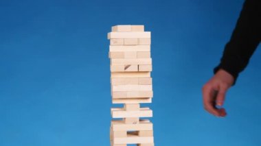 eller genç adam çalış jenga üzerinde mavi arka plan, yakın çekim. Bir adam bir kule bloklar jenga oynarken oluşturur