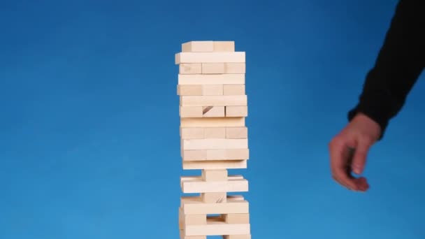 Manos de Joven juega jenga sobre fondo azul, de cerca. Un hombre construye una torre de bloques mientras juega jenga — Vídeos de Stock