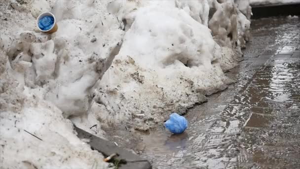 Water flows from the melting snow flowing along the asphalt. Spring melting snow. — Stock Video