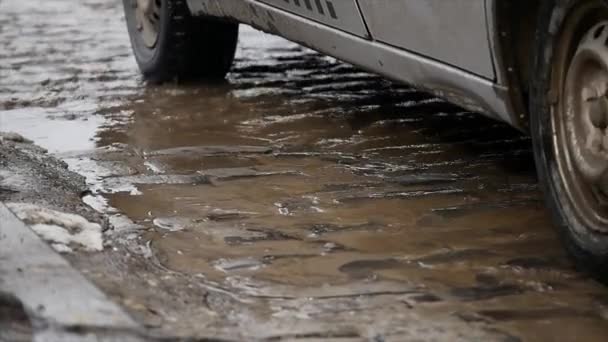 MOTION LENT, FERMER : L'eau trouble éclabousse la route asphaltée alors que la voiture roule dans la flaque d'eau. Sprays liquides marron à travers la rue noire — Video