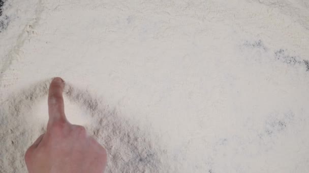 Doigt écrire COOK sur un fond de farine blanche. vue du dessus 4k — Video