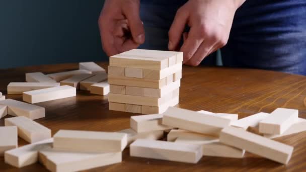 Manos de Joven juega jenga sobre fondo azul, de cerca. Un hombre construye una torre de bloques mientras juega jenga — Vídeo de stock