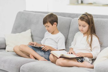kız kardeşi evde kanepenin üzerine bir kitap okur iken küçük sevimli çocuk oyun tablet