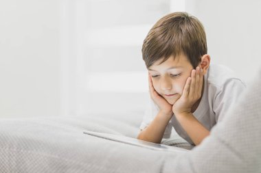 Mutlu çocuk çocuk kanepe üzerinde bir parlak güneşli rahatlatıcı kanepe izlerken tablet üzerinde oturan aktif küçük çocuk demek, çocuk teknoloji kavramı ile