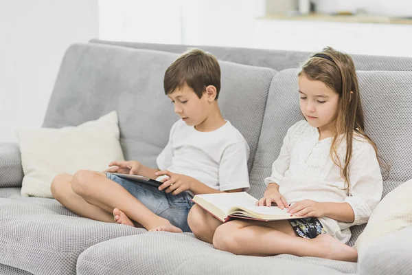 kız kardeşi evde kanepenin üzerine bir kitap okur iken küçük sevimli çocuk oyun tablet