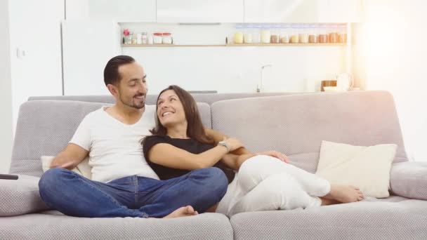 Das Paar sitzt zu Hause auf der Couch und schaut fern. Paar schaut einander verliebt an — Stockvideo
