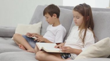 kız kardeşi evde kanepenin üzerine bir kitap okur iken küçük sevimli çocuk oyun tablet