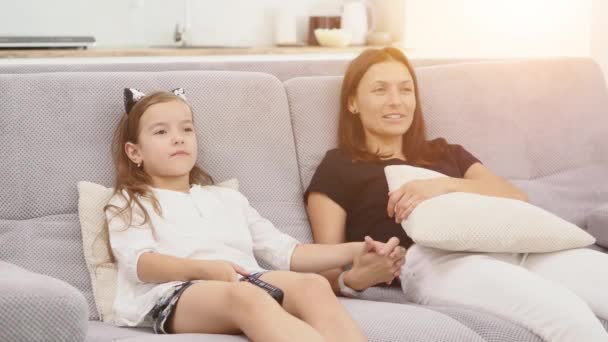 Madre e figlia si stanno divertendo molto e stanno parlando mentre guardano la TV in soggiorno seduti sul divano. madre e figlia che si tengono per mano. Da vicino. — Video Stock