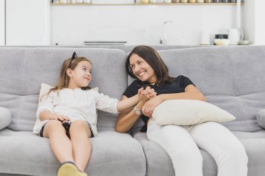 Anne ve kızı gri kanepede oturan oturma odasında çok eğlenceli olacak. Anne ve kızı elele