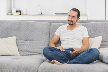 Büyük Tv programı. Uzaktan kumanda tutarak ve evde kanepede otururken Tv izlerken neşeli yakışıklı genç