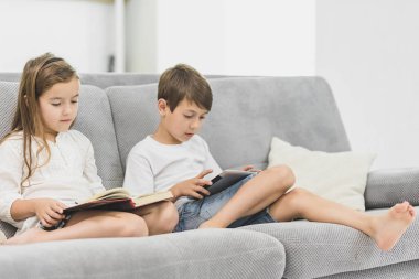 kız kardeşi evde kanepenin üzerine bir kitap okur iken küçük sevimli çocuk oyun tablet