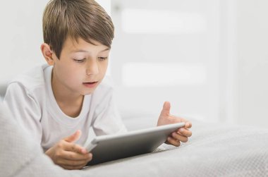 Mutlu çocuk çocuk kanepe üzerinde bir parlak güneşli rahatlatıcı kanepe izlerken tablet üzerinde oturan aktif küçük çocuk demek, çocuk teknoloji kavramı ile