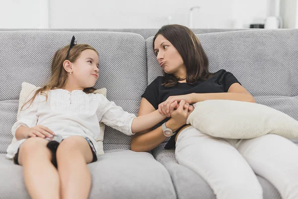 Madre e hija se están divirtiendo mucho en la sala de estar sentadas en el sofá gris. madre e hija cogidas de la mano — Foto de Stock