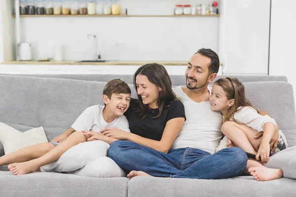 Familia sentada en el sofá sonriendo a la cámara en el moderno fondo del apartamento —  Fotos de Stock