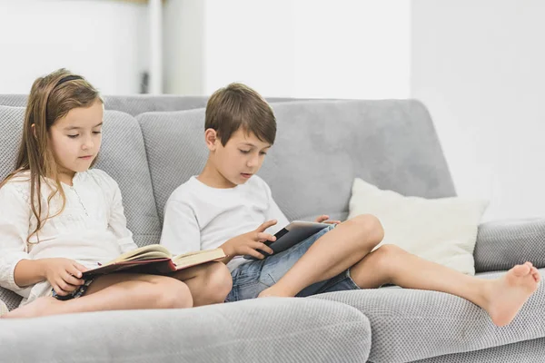 kız kardeşi evde kanepenin üzerine bir kitap okur iken küçük sevimli çocuk oyun tablet