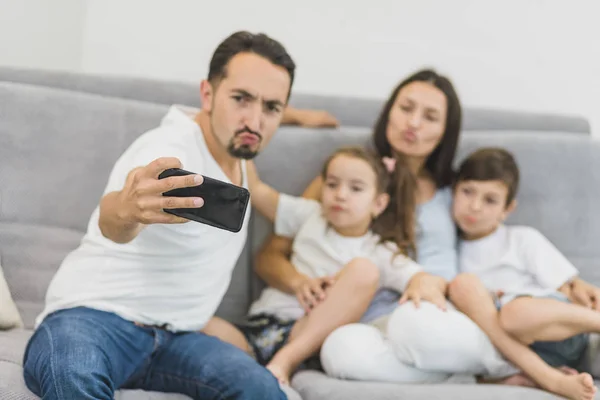 家里人坐在沙发上拍自拍照片。母亲、父亲和儿子带着智能手机自拍。快乐的父母坐在沙发上与孩子 — 图库照片
