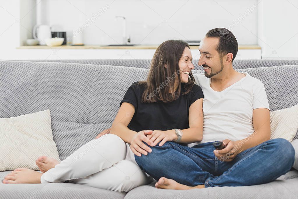 Happy family watches television while sitting on the sofa. couple in casual clothes on modern grey sofa. Loving couple looks at each other
