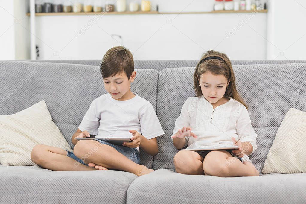 Two kids with gadgets. Sister and brother surfing the net or playing online games on digital tablets at home. Modern communication and gadget addiction concept