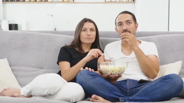 Un par de amantes ven la televisión abrazada en el sofá de la nueva casa y ven una película juntos. Concepto de: ocio, relax, tv . — Vídeo de stock