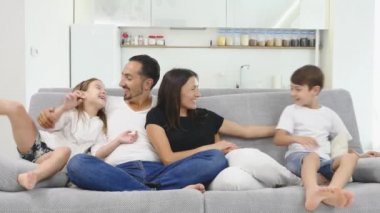 Mutlu genç aile kanepede oturan. Mutlu bir aile evde birlikte vakit. Annesi, babası, oğlu, kızı