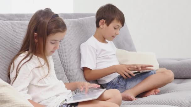 Dois miúdos com engenhocas. Irmã e irmão navegando na rede ou jogando jogos online em tablets digitais em casa. Vista lateral — Vídeo de Stock