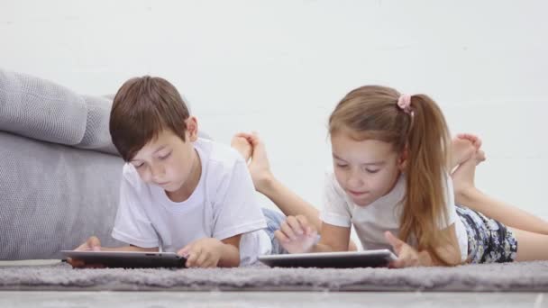 两个有小玩意的孩子姐姐和弟弟在网上冲浪或玩在线游戏的数字平板电脑在家里。现代通信与小工具成瘾概念 — 图库视频影像
