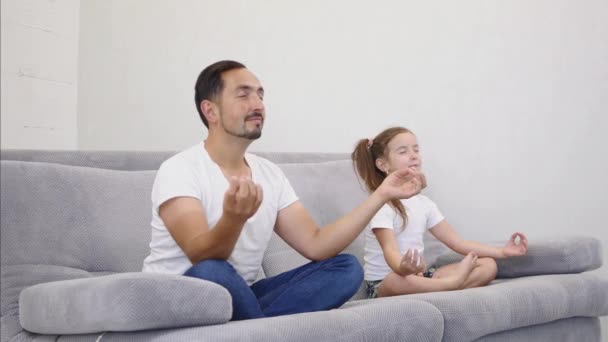 Feliz y hermoso padre joven wih hija descansando y meditando en el sofá en casa. Vista lateral — Vídeos de Stock