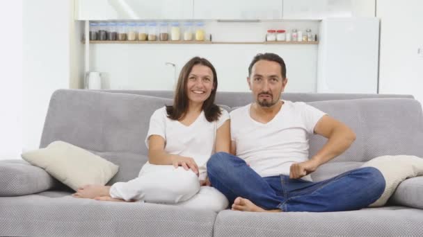 Счастливая семья с кукурузой сидела на диване в гостиной и смеялась, глядя телевизор. дети приносят миску попкорна — стоковое видео