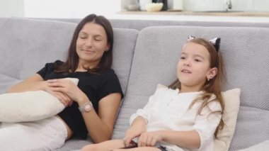 Anne ve kızı çok eğleniyorum ve oturma odasında kanepede oturup Tv izlerken konuşuyor