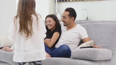 Güzel, genç ebeveynler ve çocukları televizyon izliyor, patlamış mısır yiyor ve evde kanepede otururken gülümsüyorlar.