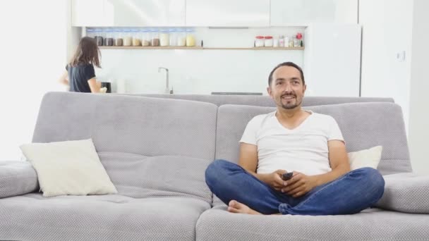 Junges Paar vor dem Fernseher mit Popcorn im Wohnzimmer. junge Frau bringt Popcorn auf die Couch — Stockvideo
