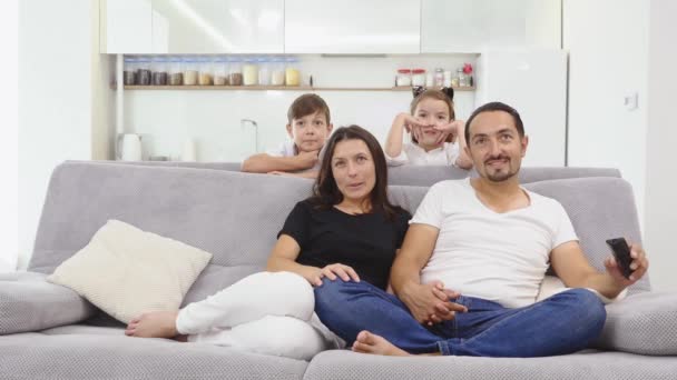 Счастливая семья сидит на диване и смотрит телевизор — стоковое видео