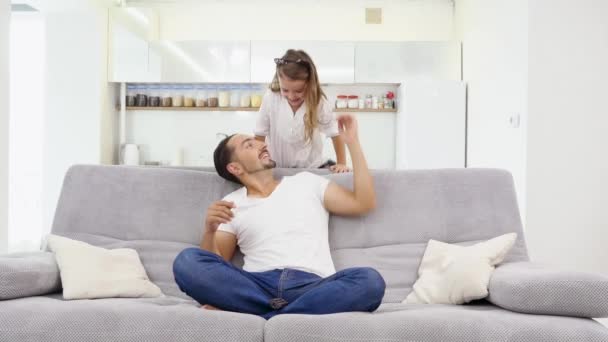 Батько грає з дочкою на дивані вдома. батько і дочка танцюють на дивані — стокове відео