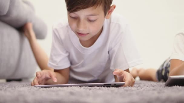 Duas crianças felizes deitadas no chão e brincando com tablet — Vídeo de Stock