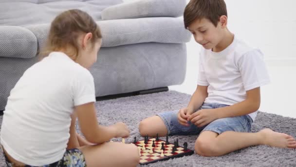 Deux petits enfants jouant aux échecs dans la chambre domestique sur le sol. Vue latérale — Video