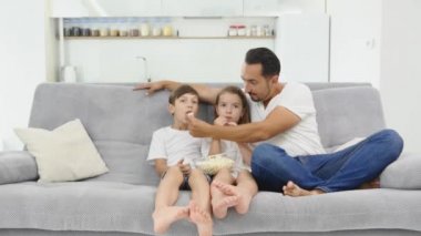 Babası kızı ve oğlu ile rahat kanepede oturan ve Tv. kapalı izlerken patlamış mısır ile gülümsedi