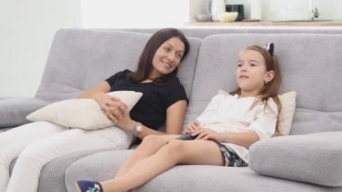 Anne ve kızı çok eğleniyorum ve oturma odasında kanepede oturup Tv izlerken konuşuyor. Anne ve kızı elele. Anne kızı el öper..