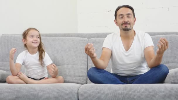 Счастливый и красивый молодой папа с дочерью отдыхает и медитирует на диване дома. Вид спереди — стоковое видео