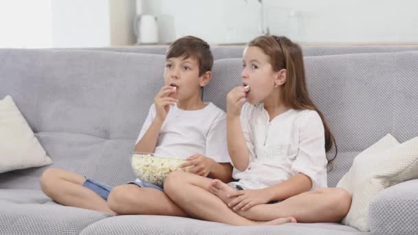 Брат з сестрою їсть попкорн вдома — стокове відео