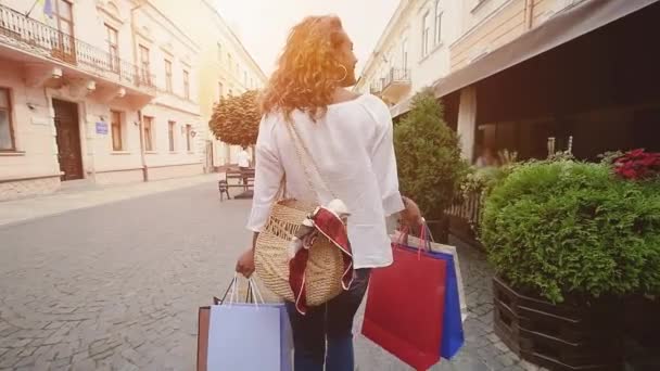 Achteraanzicht van lokale meisje wandelen langs stad straat met boodschappentassen na het kopen van veel van nieuwe kleren slow motion — Stockvideo