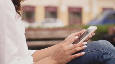 Kadın parkta bankta oturmuş telefonuna bir mesaj yazmaya. Yakın çekim yakışıklı
