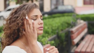 Bir bankta açık havada güneşli bir günde oturan genç güzel dalgın kahverengi saçlı kadın. Kız yoruldu, baş ağrısı acı çekiyor