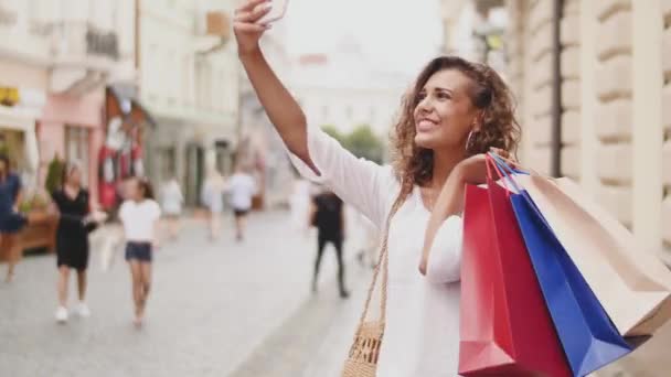 Модная счастливая молодая женщина с сумками делает фотоавтопортрет на смартфоне — стоковое видео