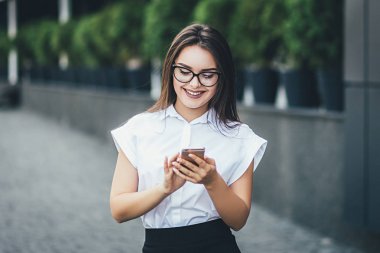 Yürüyüş ve rüzgar saçlarını bir sokakta hareket ederken bir akıllı telefon hatta sms mesajları okuma veya yazma mutlu güzel iş kadını