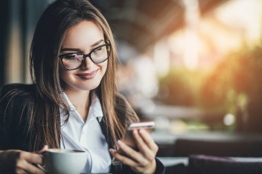 Güzel bir kadın oturuyor ve loft kafede içmeden önce sıcak kahve fincanı tutarken cep telefonu arıyorum