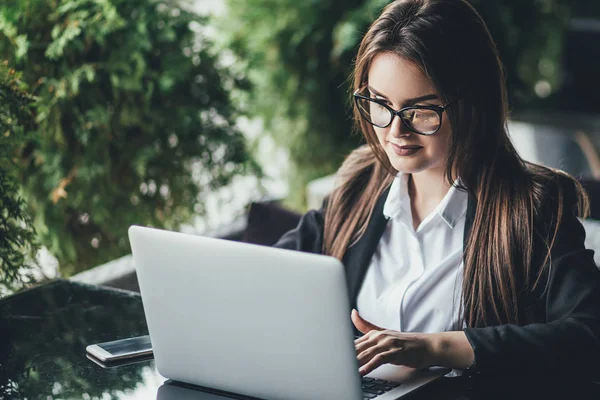 Portrait of a young beautiful girl wearing eyeglasses sitting in front of laptop at cafe. Concept of business woman — Stock Photo, Image